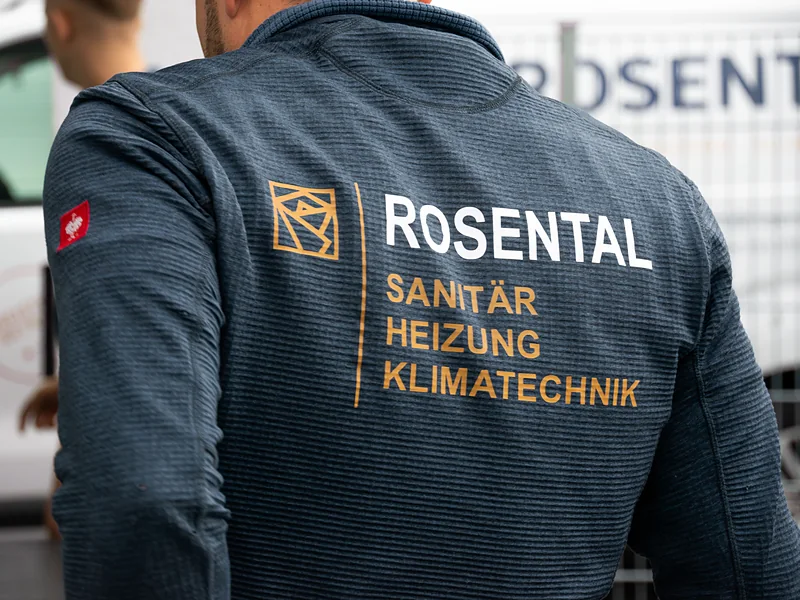 Rücken einer dunkelblauen Fleecejacke mit Rückendruck „Rosental Sanitär Heizung Klimatechnik“ in Weiß und Gold